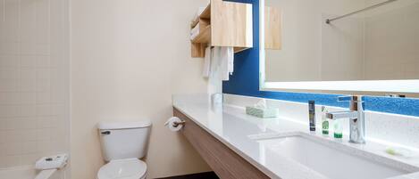 A bathroom with a toilet, sink, mirror, and wooden shelf with towels.