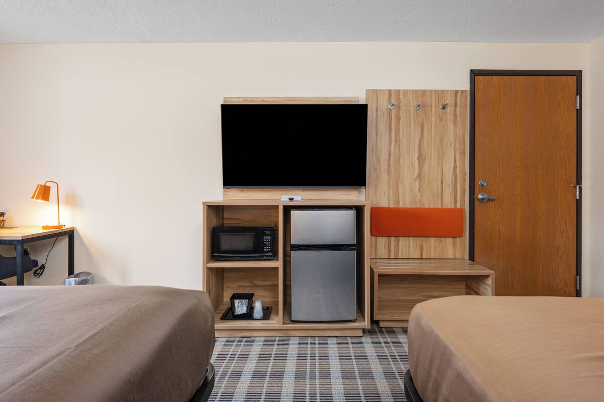 Quarto de hotel com duas camas, televisão, micro-ondas, frigorífico e guarda-roupa de madeira.