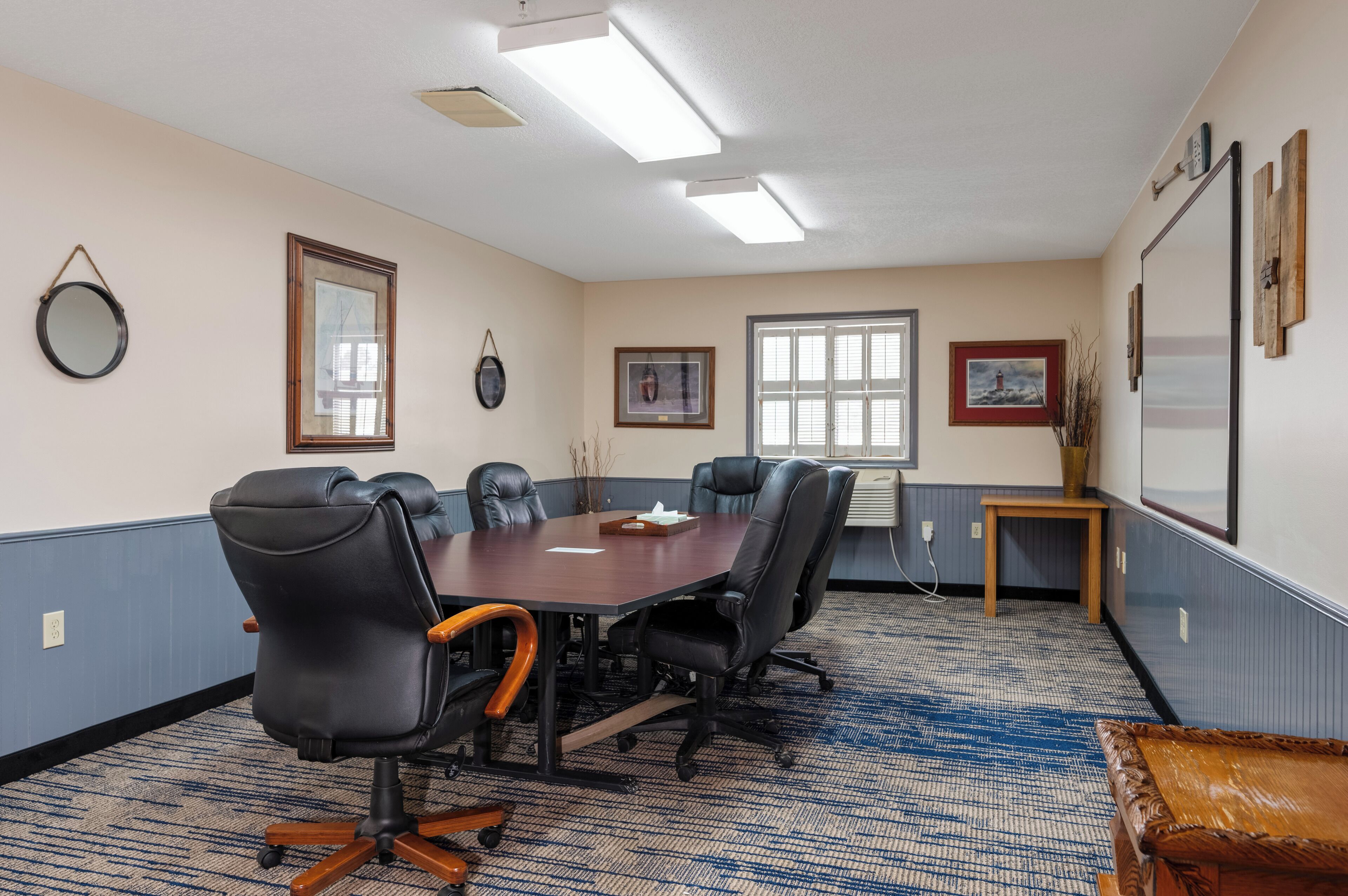 A conference room with a large table, four chairs, a small side table, and a projector screen.