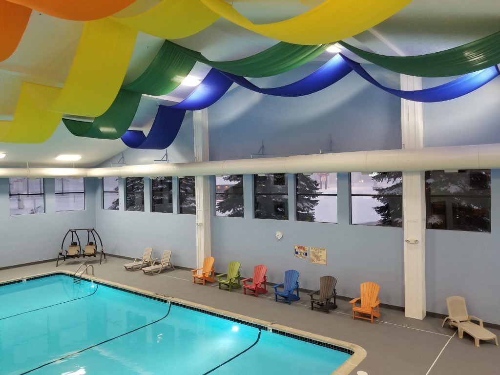 An indoor swimming pool with a clear view of the pool area, a swing chair, and several lounge chairs along the wall.