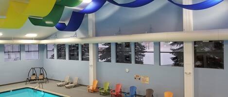 An indoor swimming pool with a clear view of the pool area, a swing chair, and several lounge chairs along the wall.