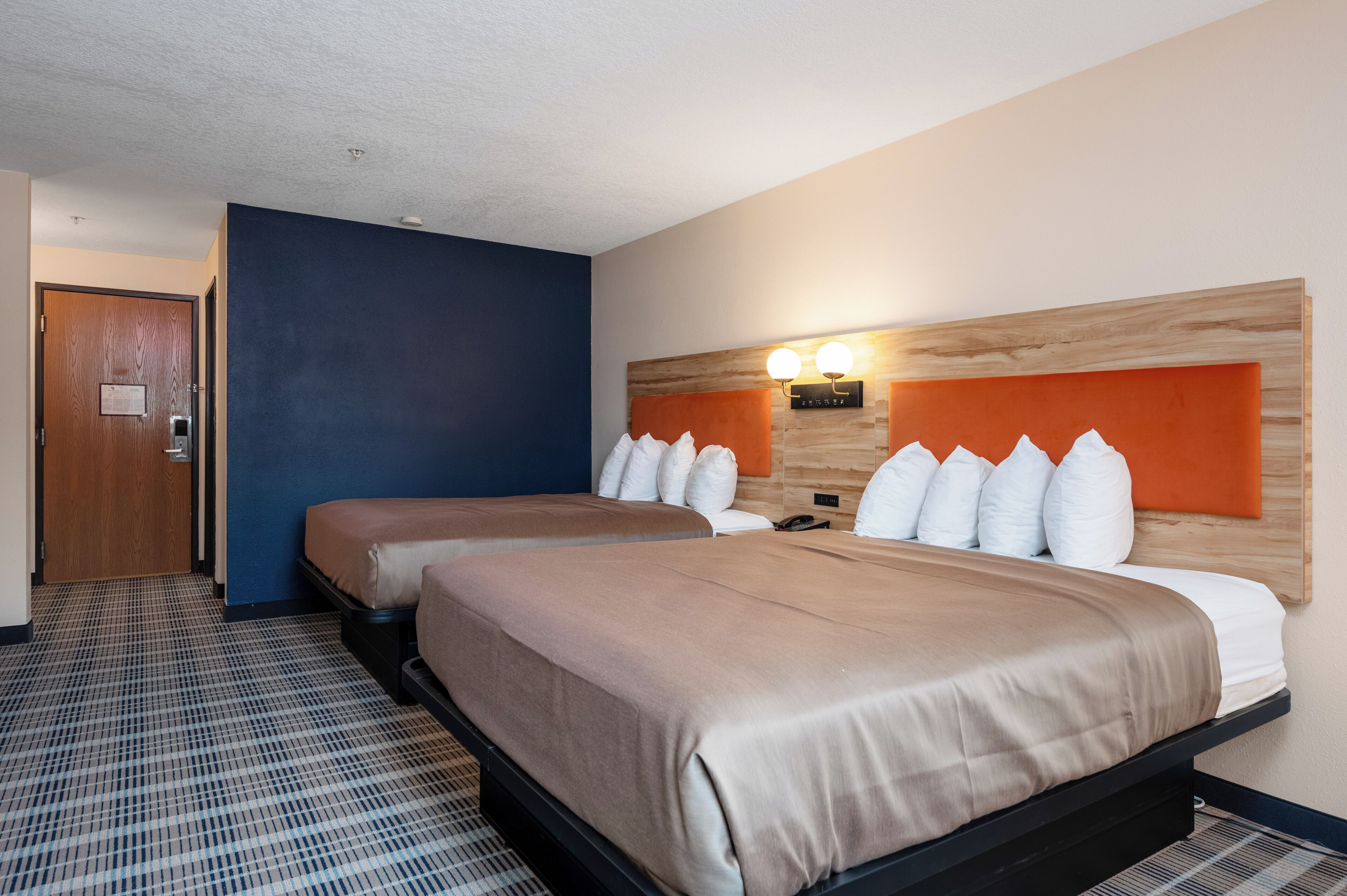 A hotel room with two beds, a wooden headboard, a patterned floor, and a door.