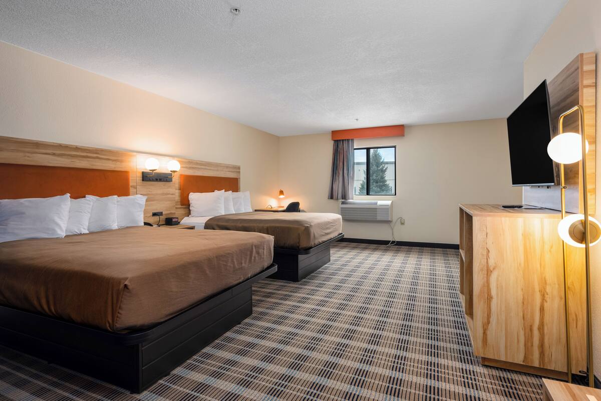 Quarto de hotel com duas camas, uma escrivaninha, uma televisão e uma janela com cortinas.