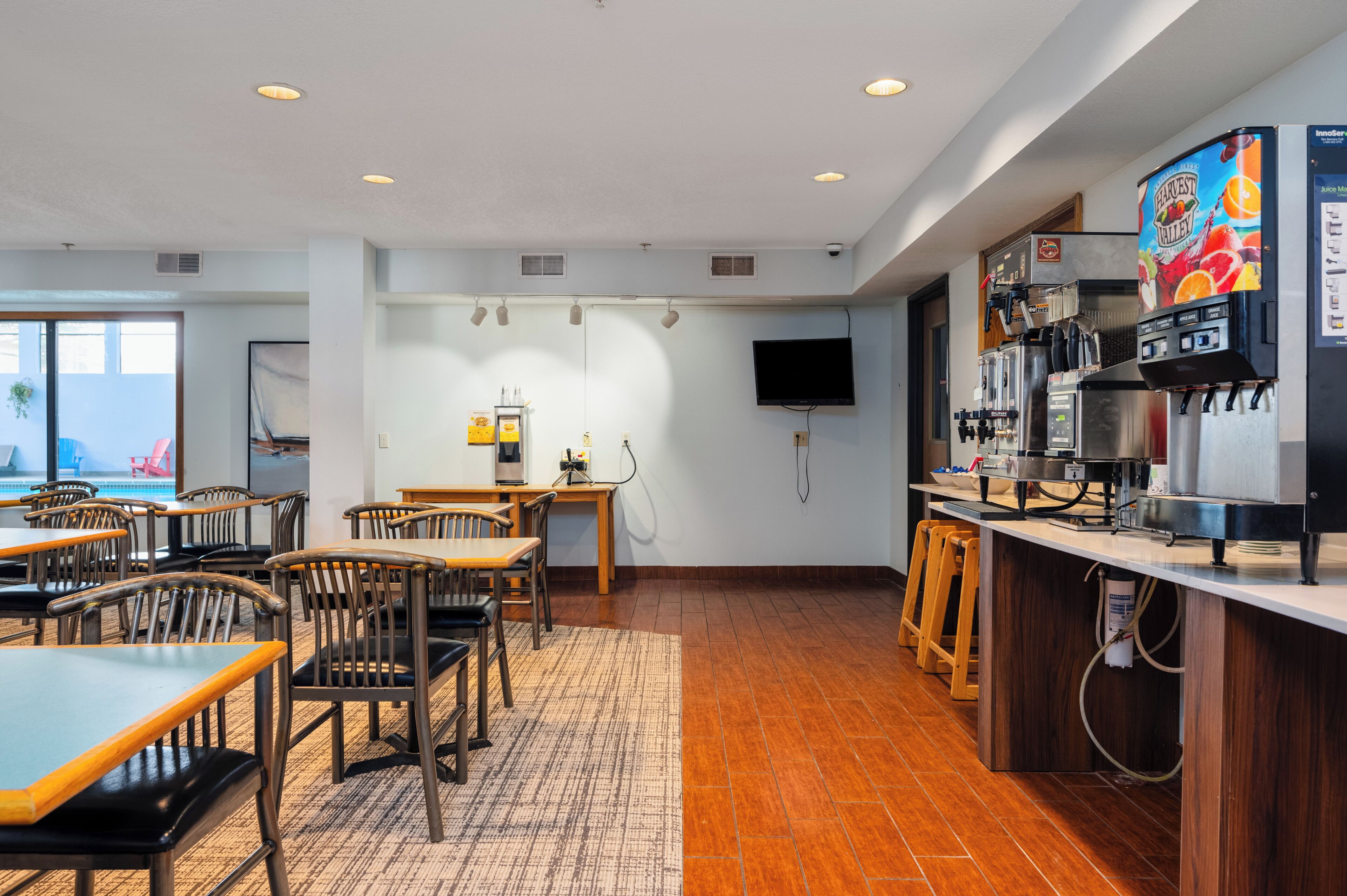 A modern hotel room with a dining area, a coffee bar, and a flat-screen TV mounted on the wall.