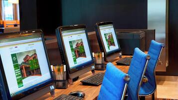A row of desktop computers with monitors displaying real estate websites, arranged on a wooden desk with blue chairs.