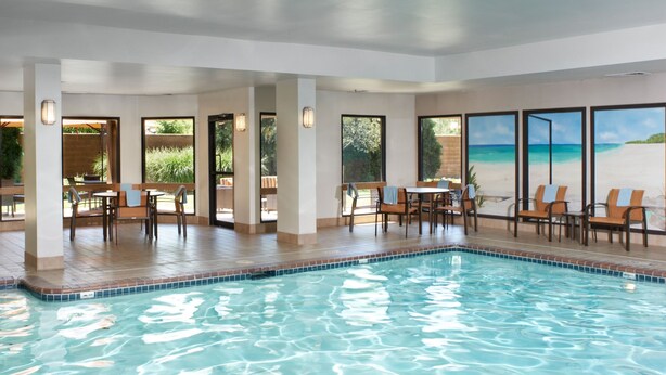 Una piscina interior con agua cristalina, rodeada de sillones de descanso y mesas, y grandes ventanales que ofrecen vistas a una playa.