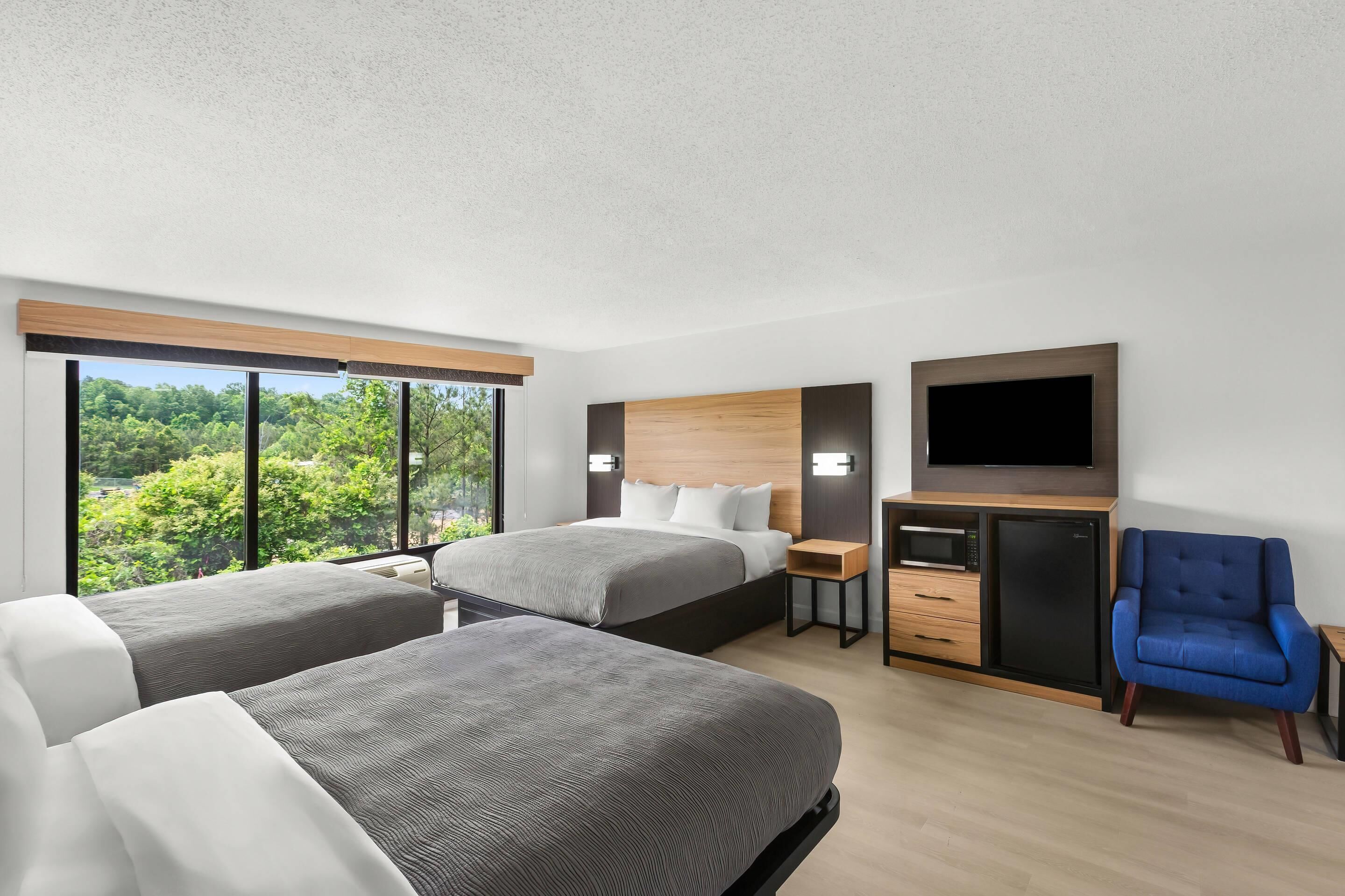 Una habitación de hotel con dos camas, un televisor, un microondas y una silla azul.