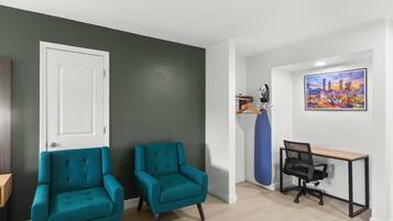 A room with two teal armchairs, a black office chair, a desk, and a cityscape painting on the wall.