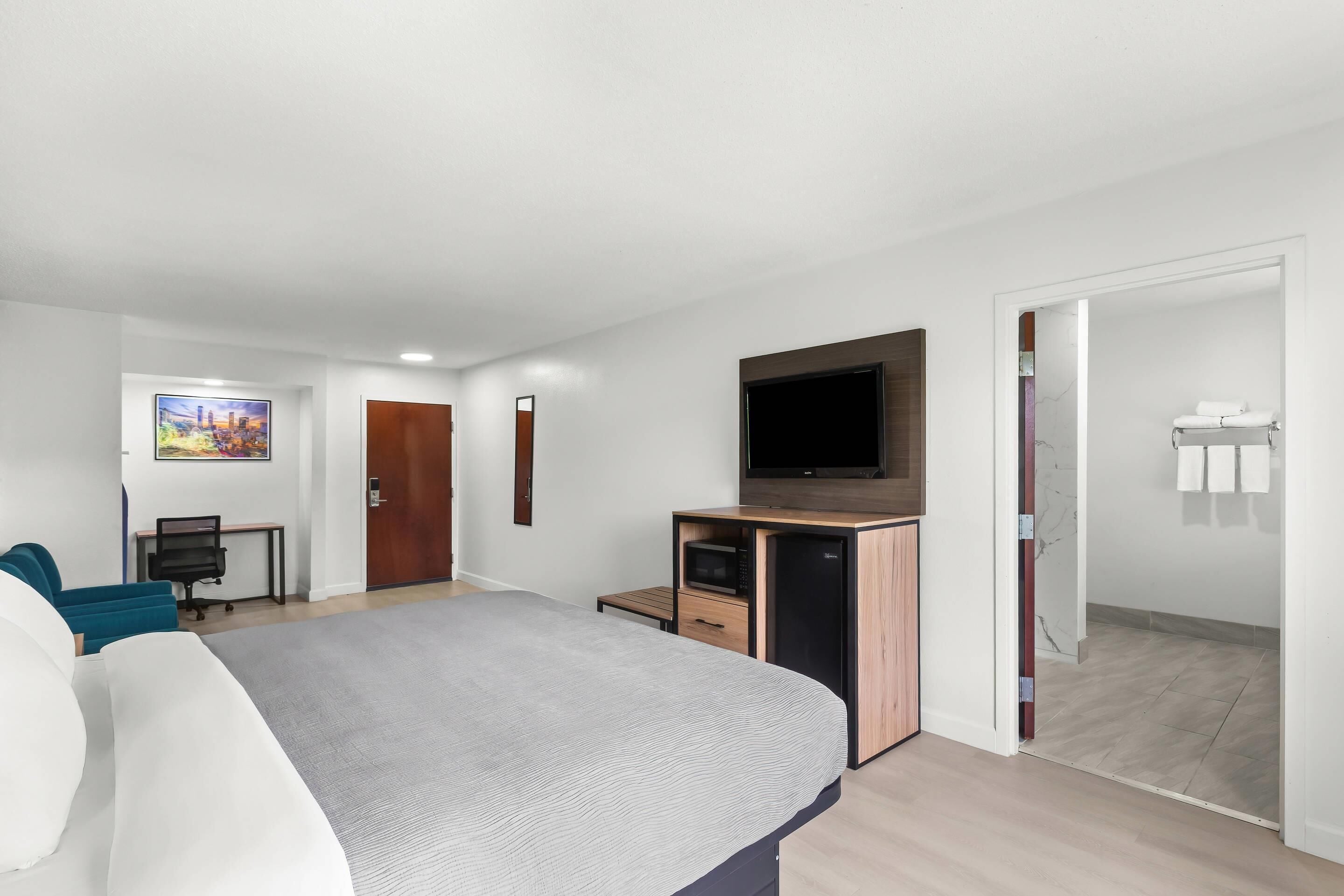 Habitación de hotel moderna con cama, escritorio, televisión y baño visible a través de una puerta abierta.
