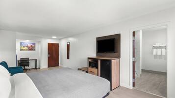 Habitación de hotel moderna con cama, escritorio, televisión y baño visible a través de una puerta abierta.