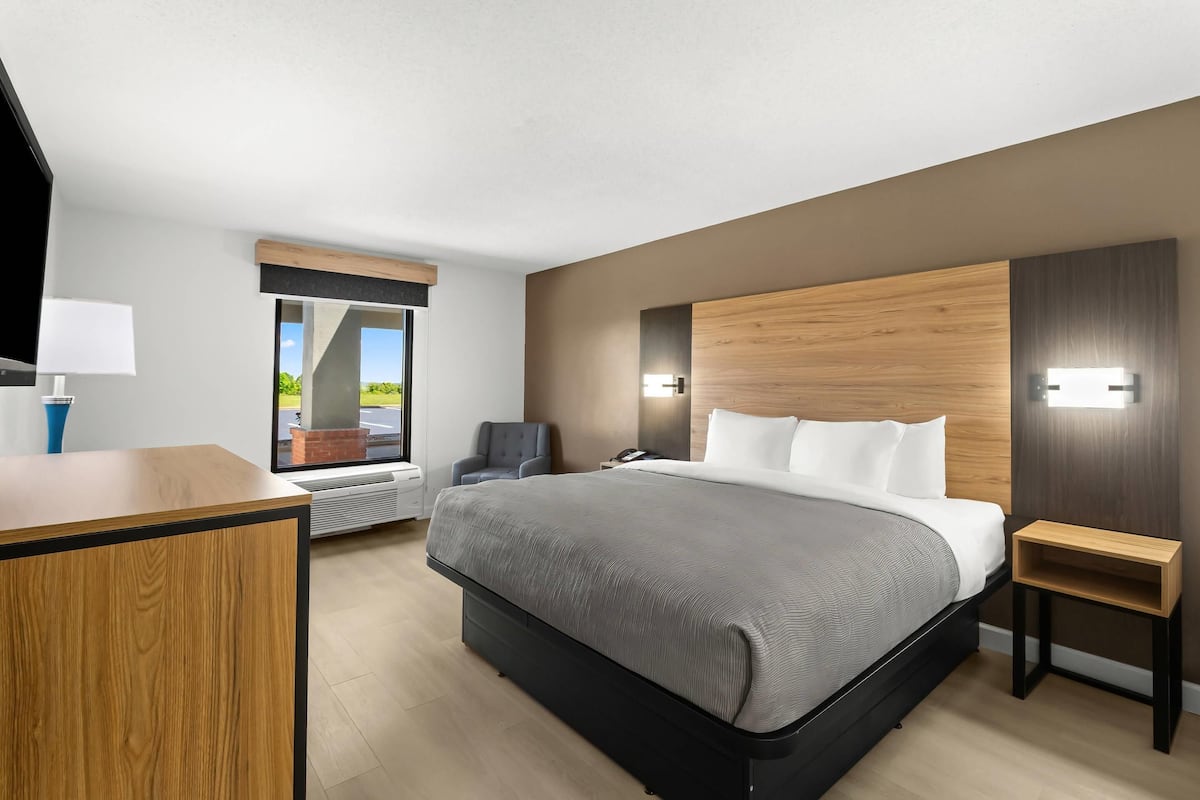 A modern hotel room with a large bed, a desk, a chair, and a view of the outdoors.