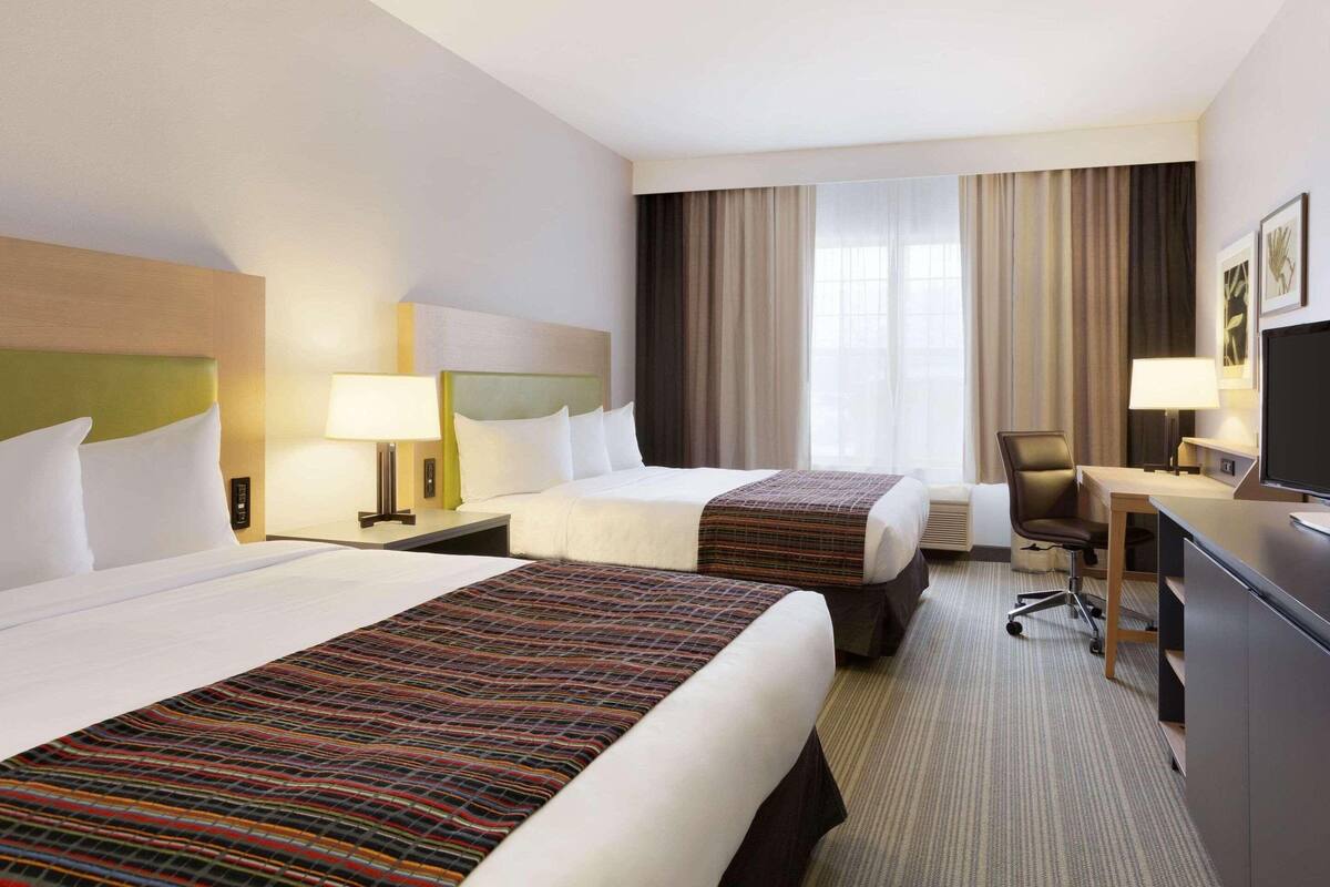 A hotel room with two beds, a desk, a chair, and a television.