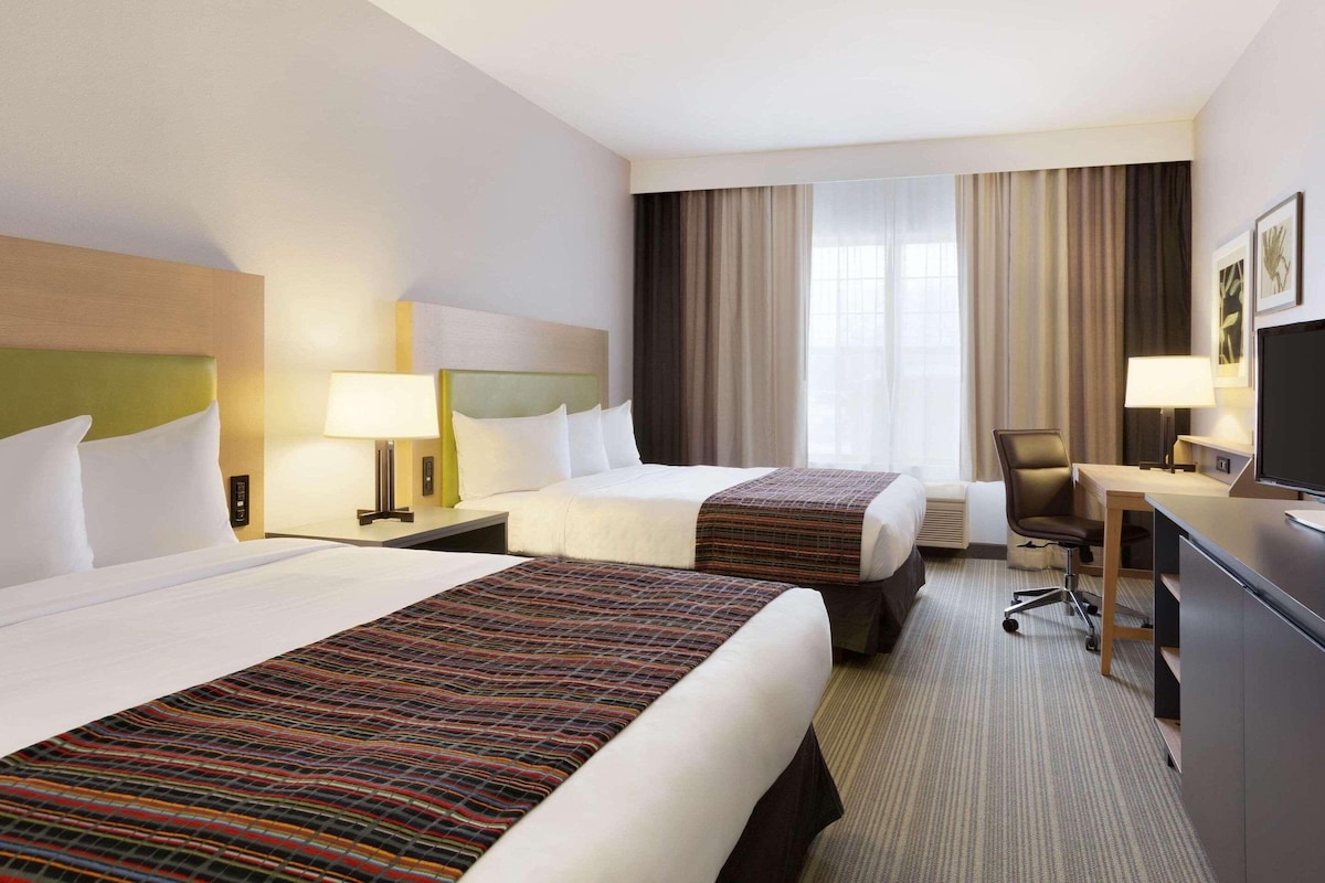 Ein Hotelzimmer mit zwei Betten, einem Schreibtisch, einem Stuhl und einem Fernseher.
