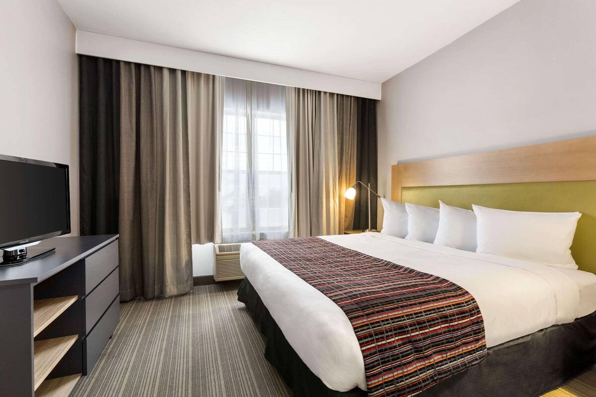 A hotel room with a bed, a television, a desk, and a window with curtains.