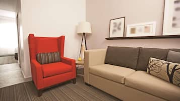 A hotel room with a red armchair, a beige sofa, a lamp, and framed pictures on the wall.