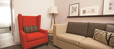 A hotel room with a red armchair, a beige sofa, a lamp, and framed pictures on the wall.