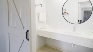 Un baño con un lavabo blanco, un espejo redondo, un perchero y una puerta con pomo negro.