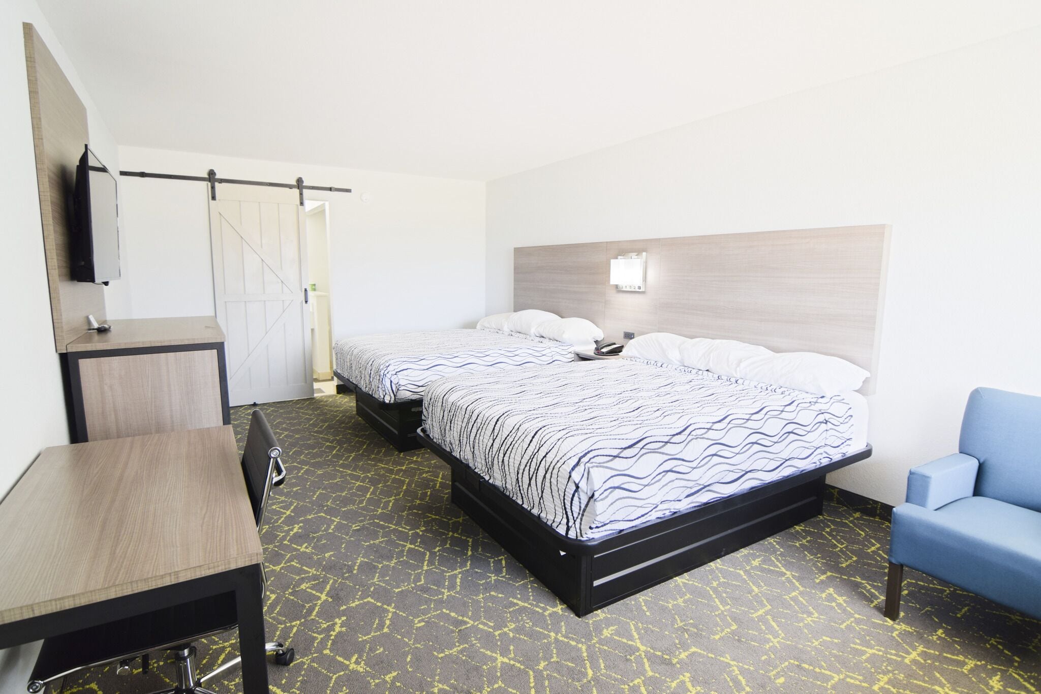 A hotel room with a bed, a desk, a chair, and a TV on the wall.