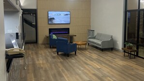 Una sala de estar moderna con piso de madera, un televisor de pantalla plana, sofás azules y grises, una mesa de centro de madera y un ventanal grande.