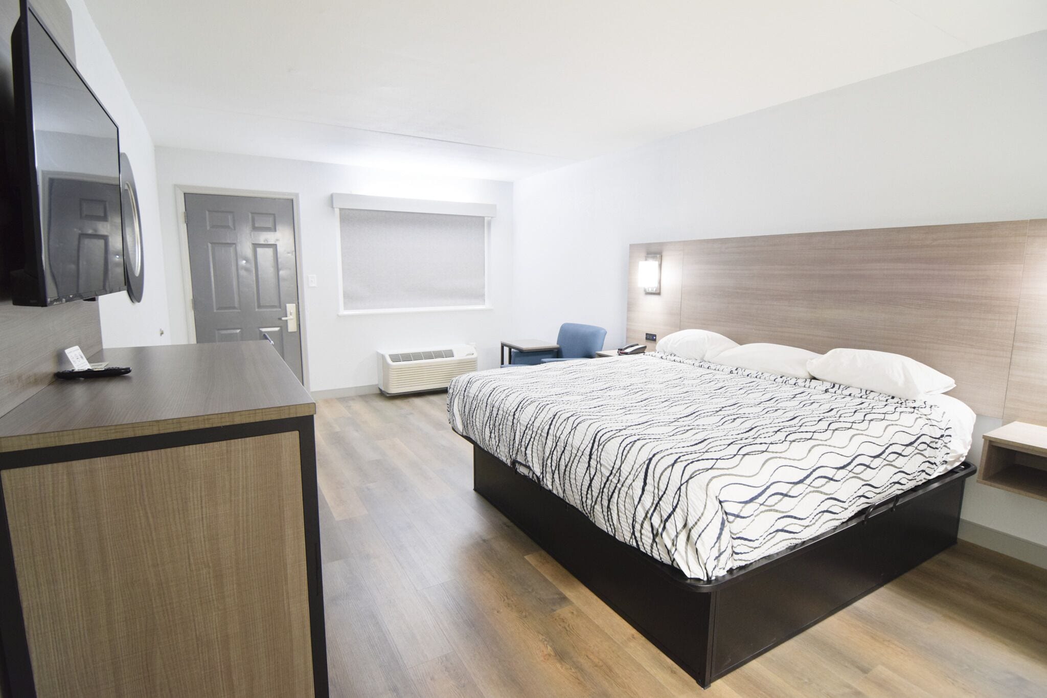 A modern hotel room with a bed, a desk, a chair, and a TV.