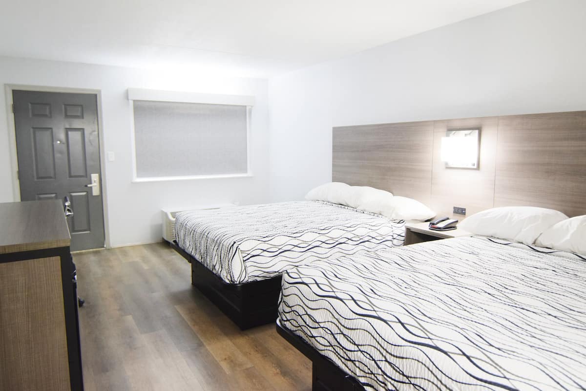 A hotel room with two beds, a desk, a window, and a door.