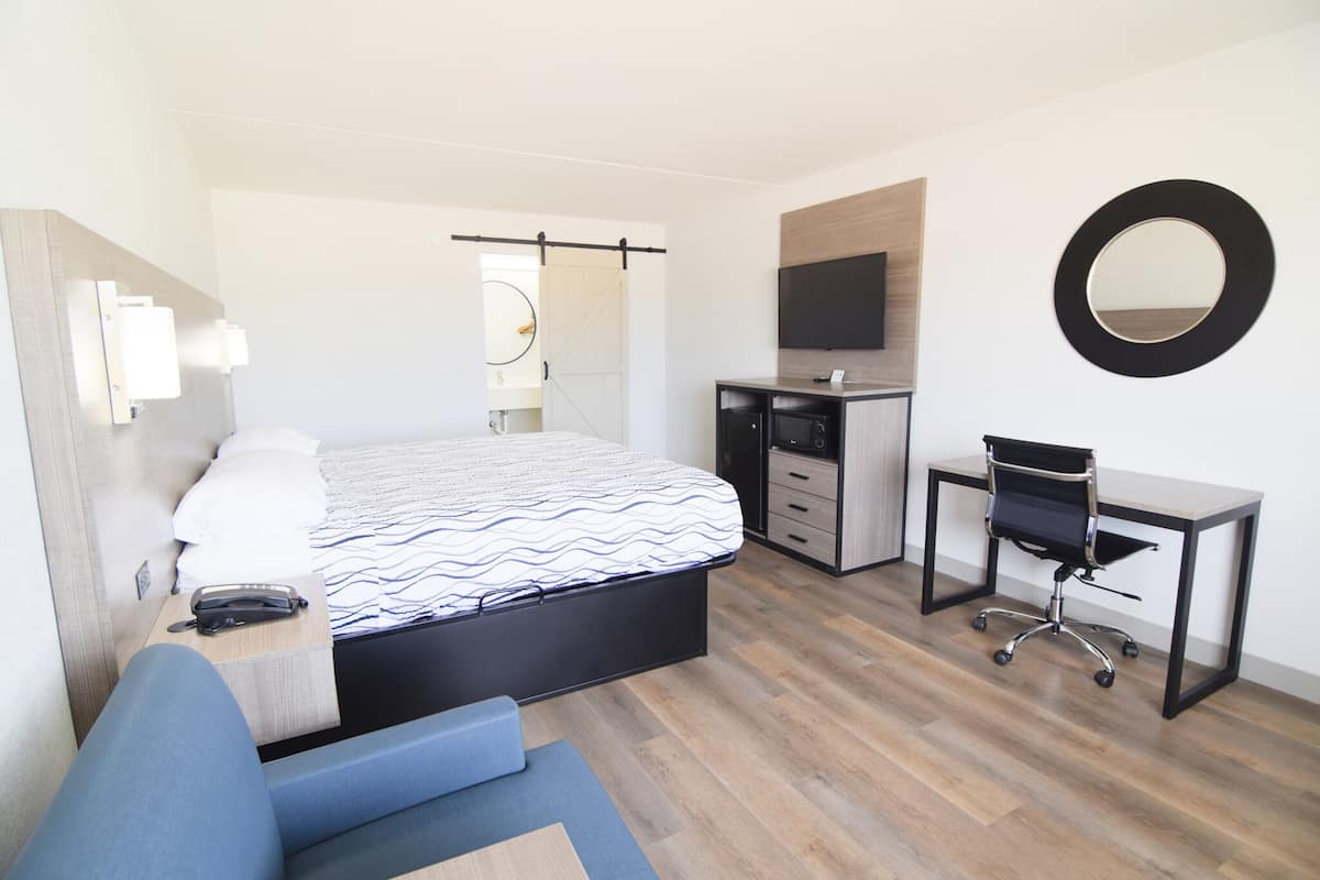 A modern hotel room with a bed, desk, chair, and a TV mounted on the wall.