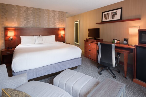 A hotel room with a large bed, a desk with a chair, a mirror, a television, and a coffee maker.