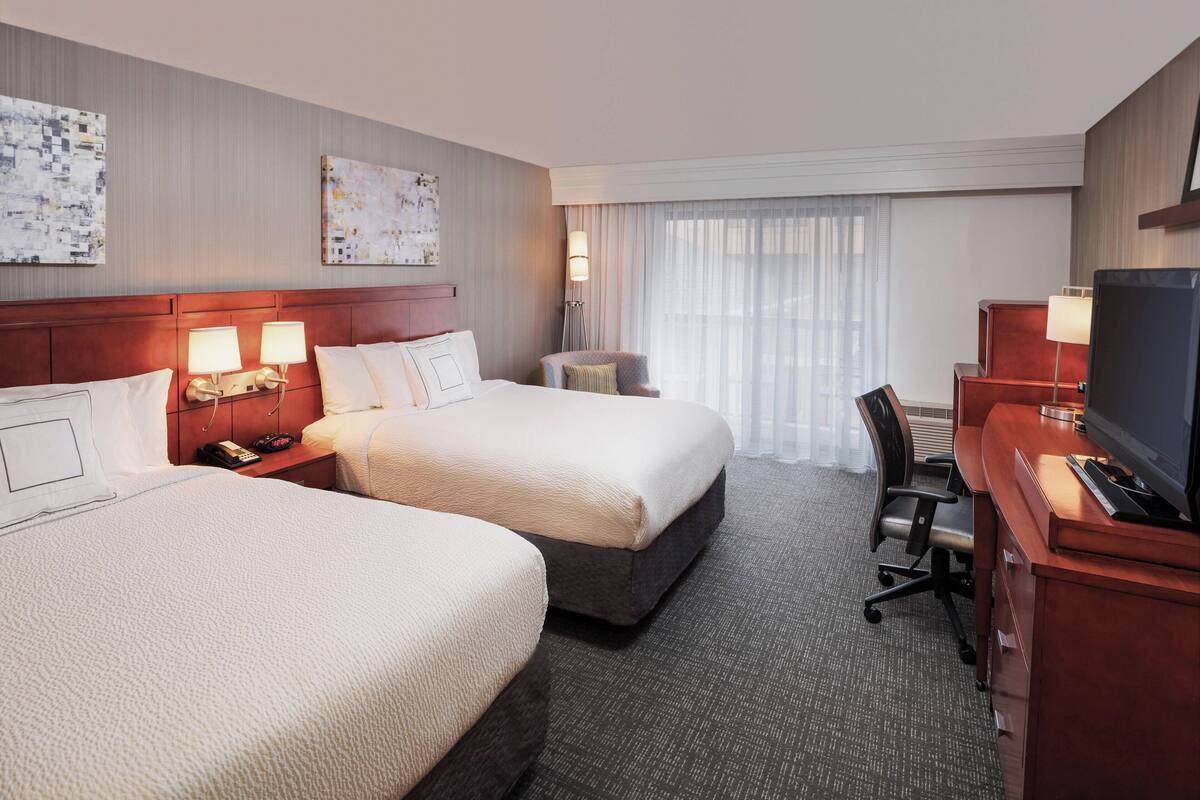 A hotel room with two beds, a desk with a TV, and a chair.