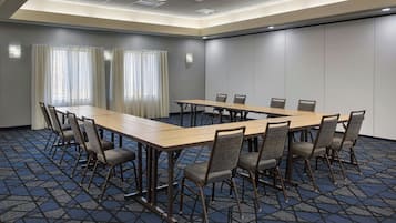 A conference room with a long table and chairs, a patterned carpet, and a plain wall with a light fixture.