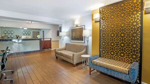 Un hall d’hôtel avec un plancher en bois, un canapé, un banc, une petite table et un panneau décoratif au mur.