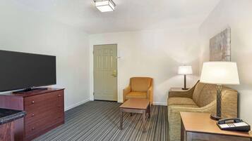 A hotel room with a flat-screen TV on a wooden dresser, a sofa, a coffee table, and a lamp.