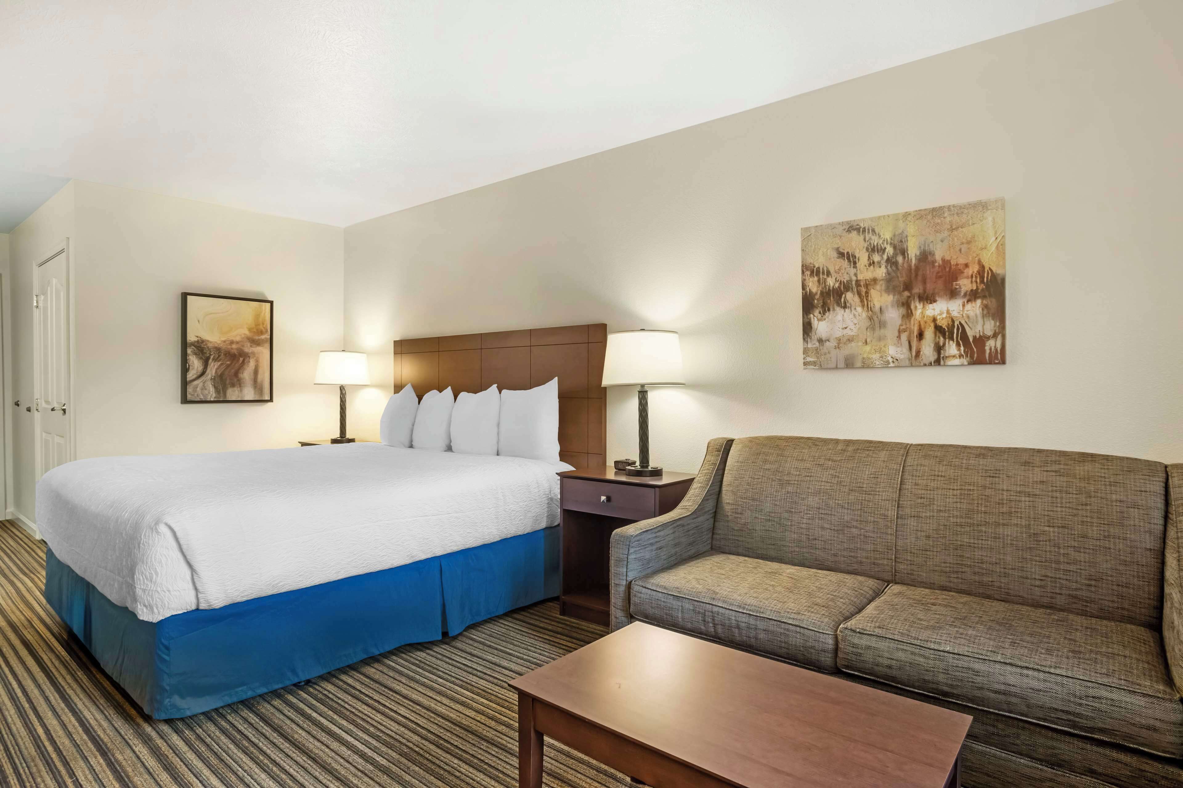A hotel room with a large bed, a sofa, a coffee table, and two lamps.