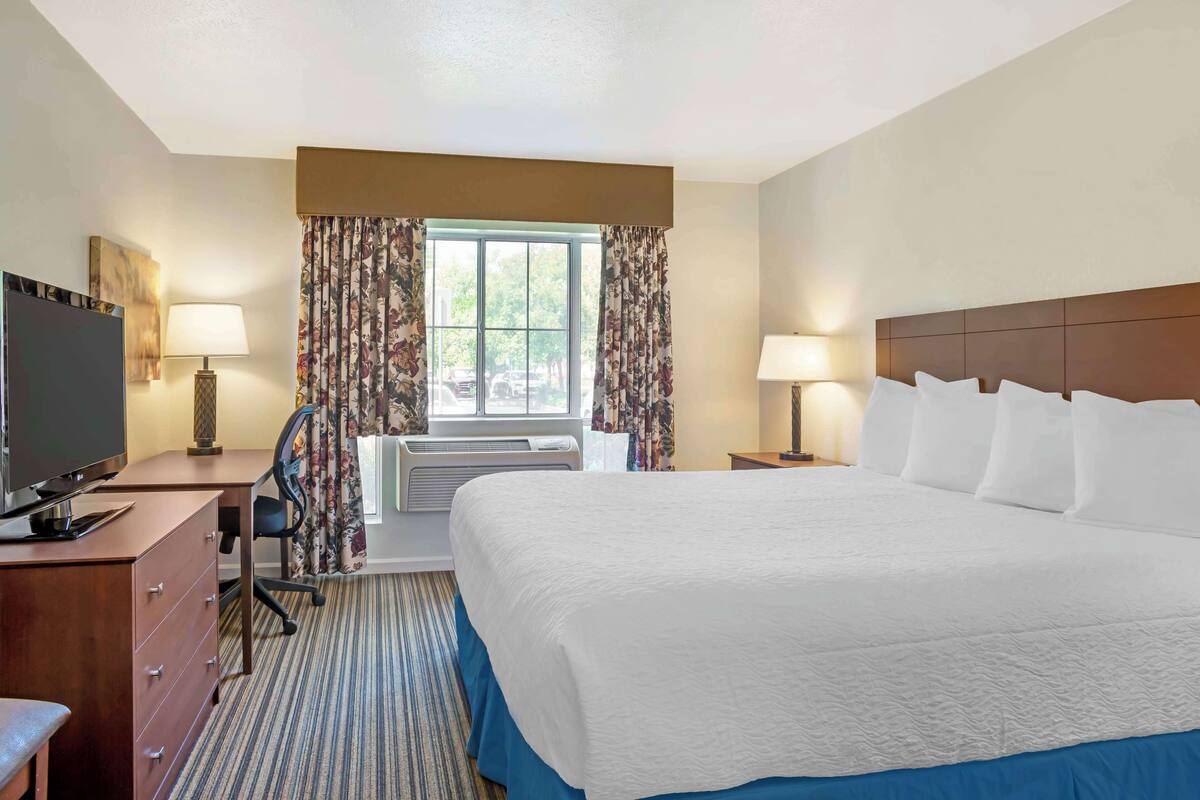 A hotel room with a large bed, a desk with a computer, a TV, and an air conditioning unit.