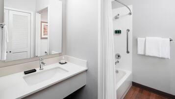 A modern bathroom with a white sink, a large mirror, a shower with a curved glass door, and a towel rack.