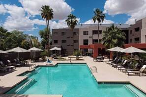 A swimming pool with lounge chairs and umbrellas, surrounded by palm trees and a building with multiple floors. - Courtyard by Marriott Scottsdale North (Phoenix)