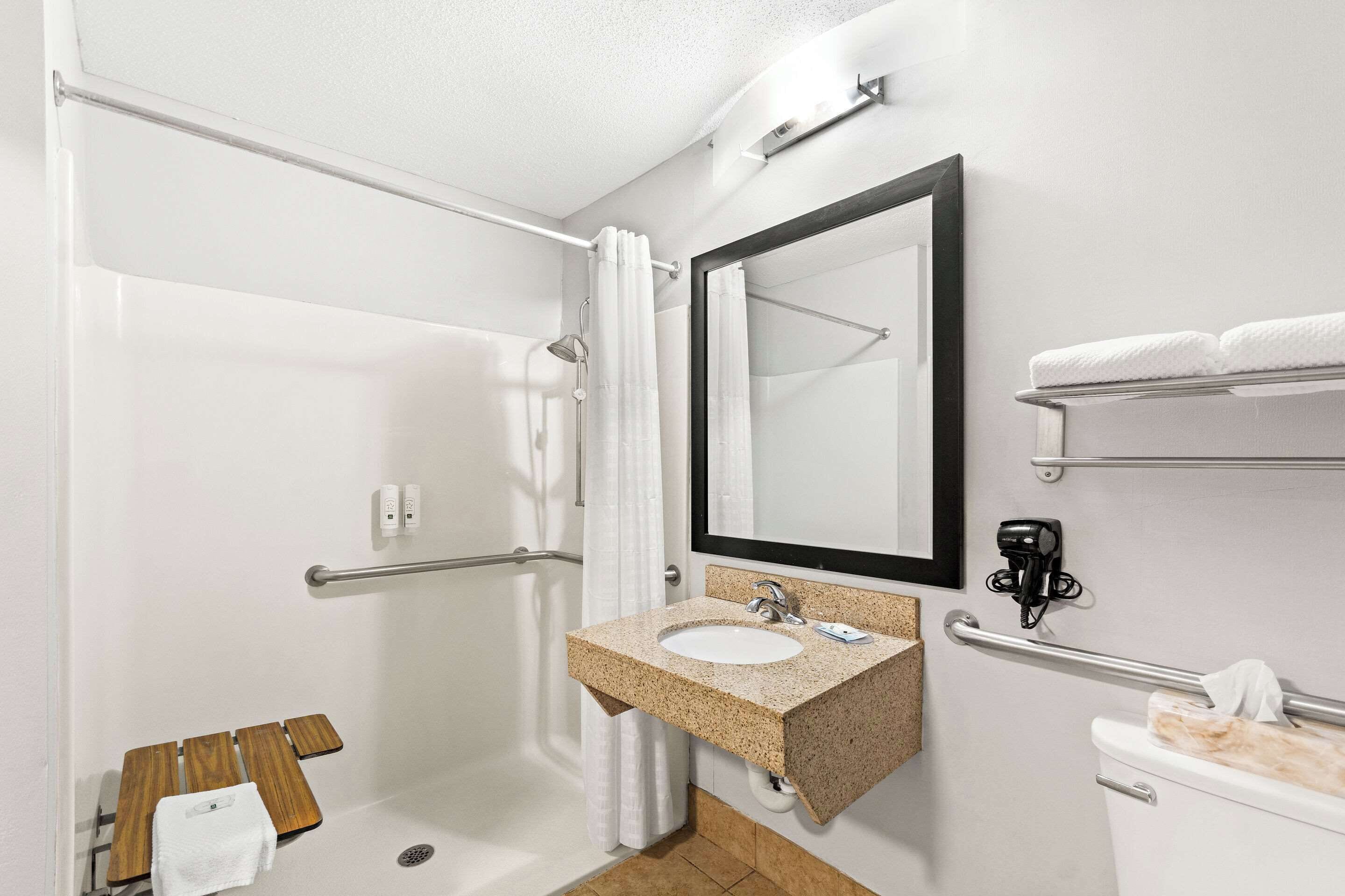 A modern bathroom with a shower, a sink with a granite countertop, a mirror, and a towel rack.