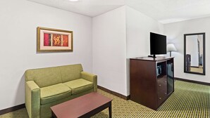 A hotel room with a green sofa, a wooden cabinet with a flat-screen TV, a small table, and a patterned carpet. - Quality Inn Dry Ridge (Dry Ridge)