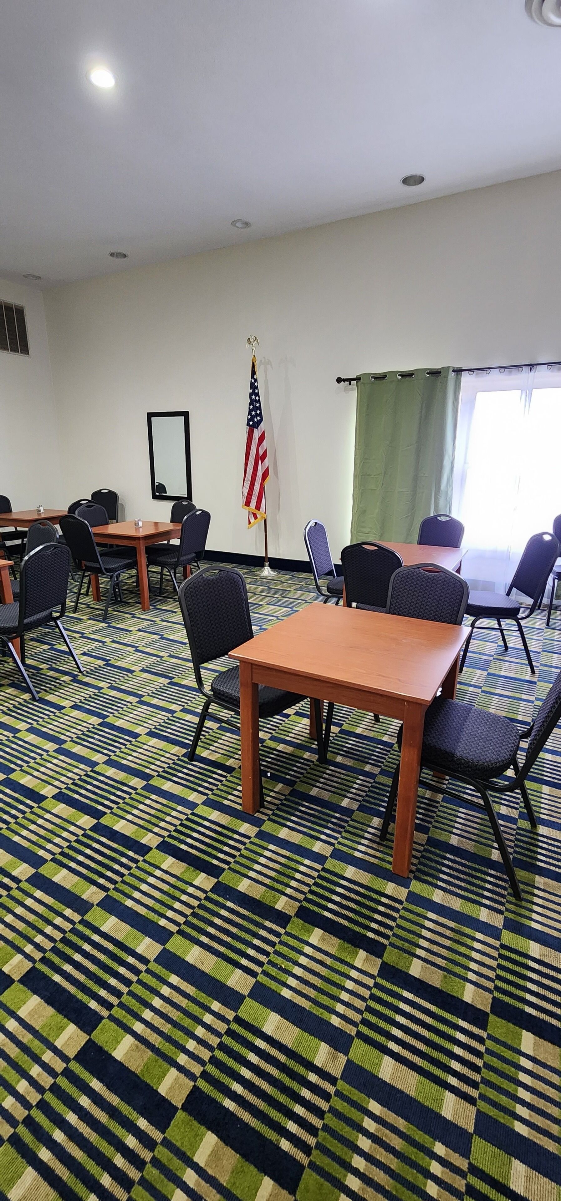 Une salle de conférence équipée de tables et de chaises, avec un drapeau américain et un tapis à motifs.