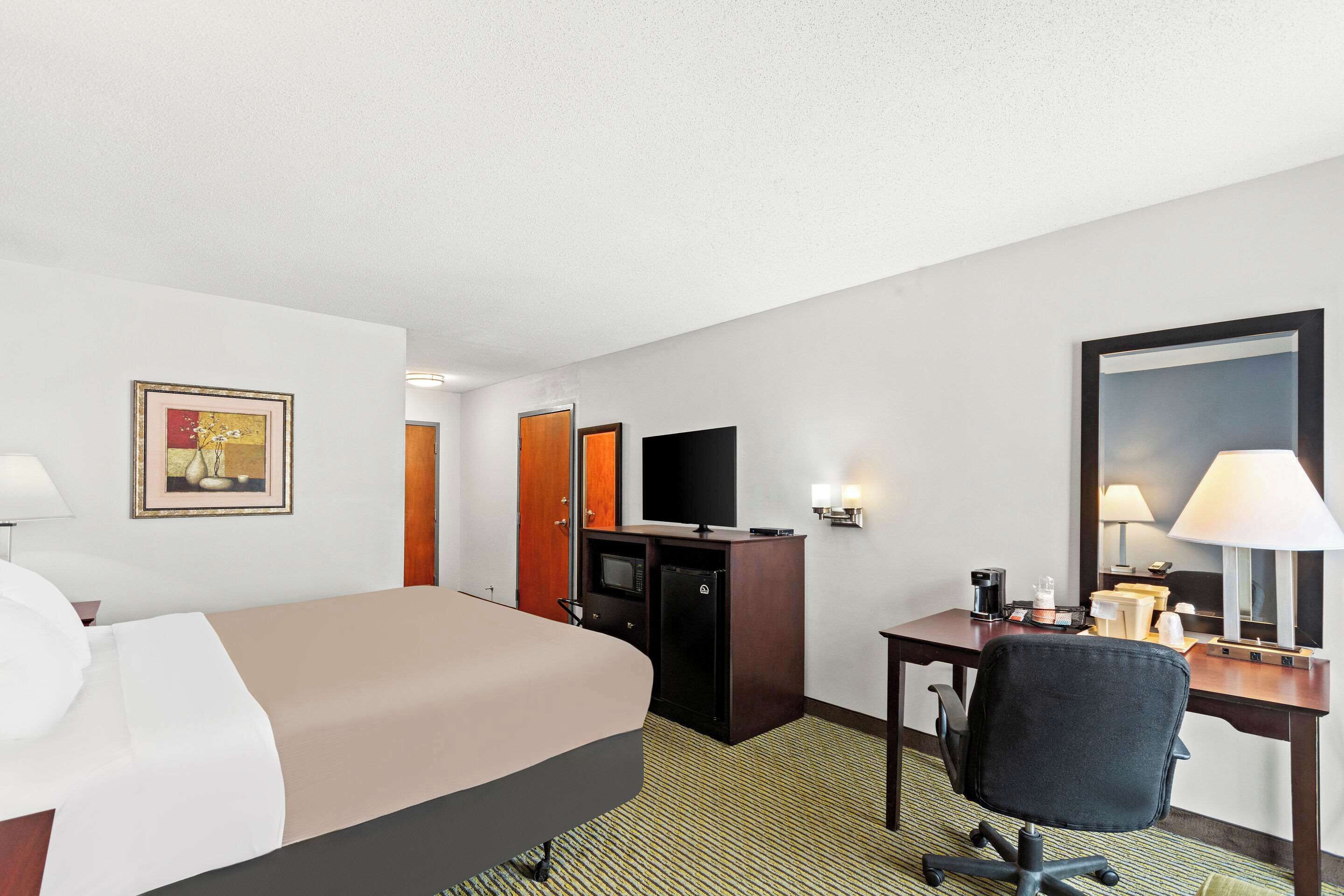 A hotel room with a bed, a desk, a TV, a refrigerator, and a mirror.