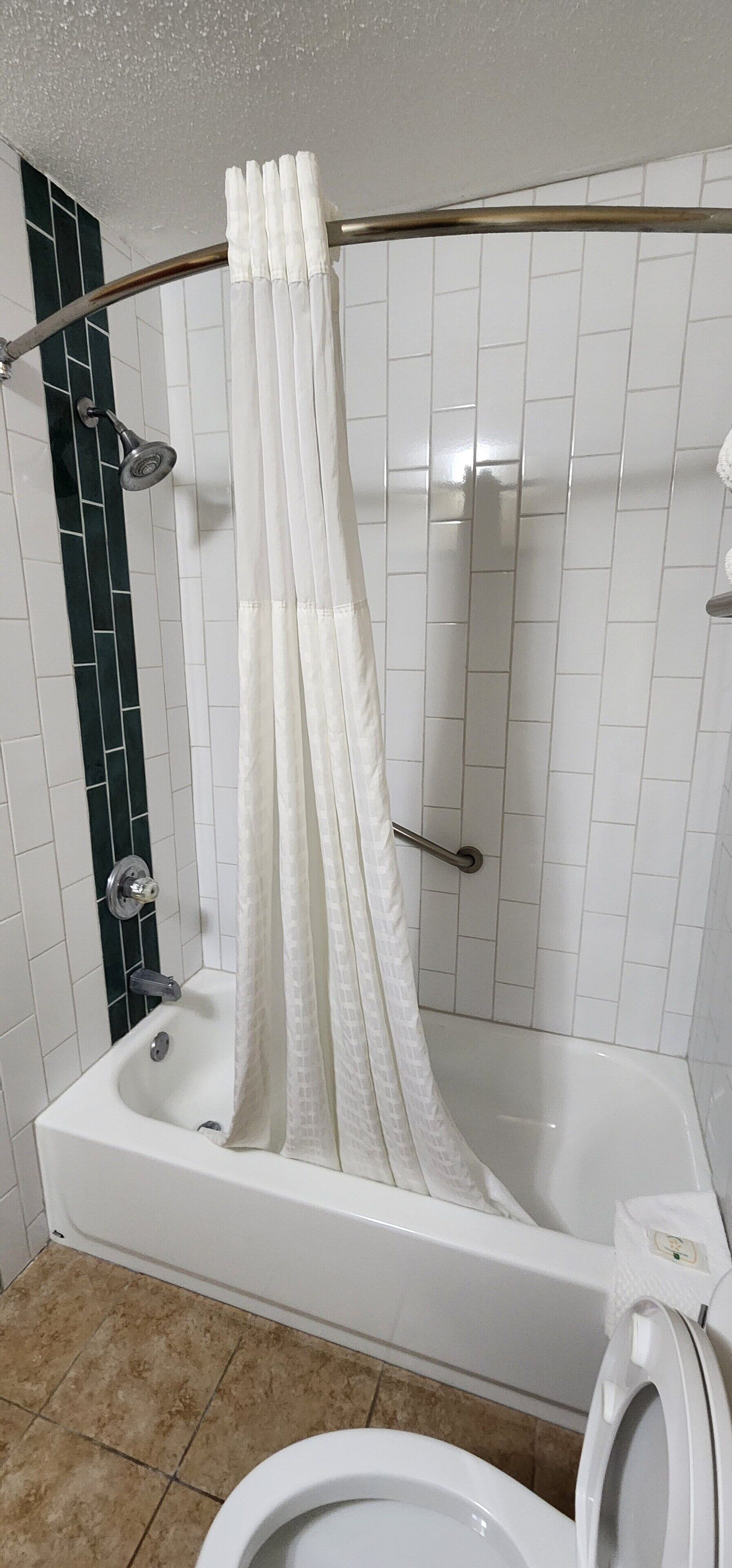 Une salle de bain équipée d’une baignoire, d’un rideau de douche, de toilettes et d’une barre d’appui.