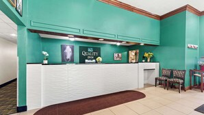 A reception desk with a sign reading "Quality Inn" and a framed horse picture. There are two chairs and a vase with yellow flowers. - Quality Inn Dry Ridge (Dry Ridge)