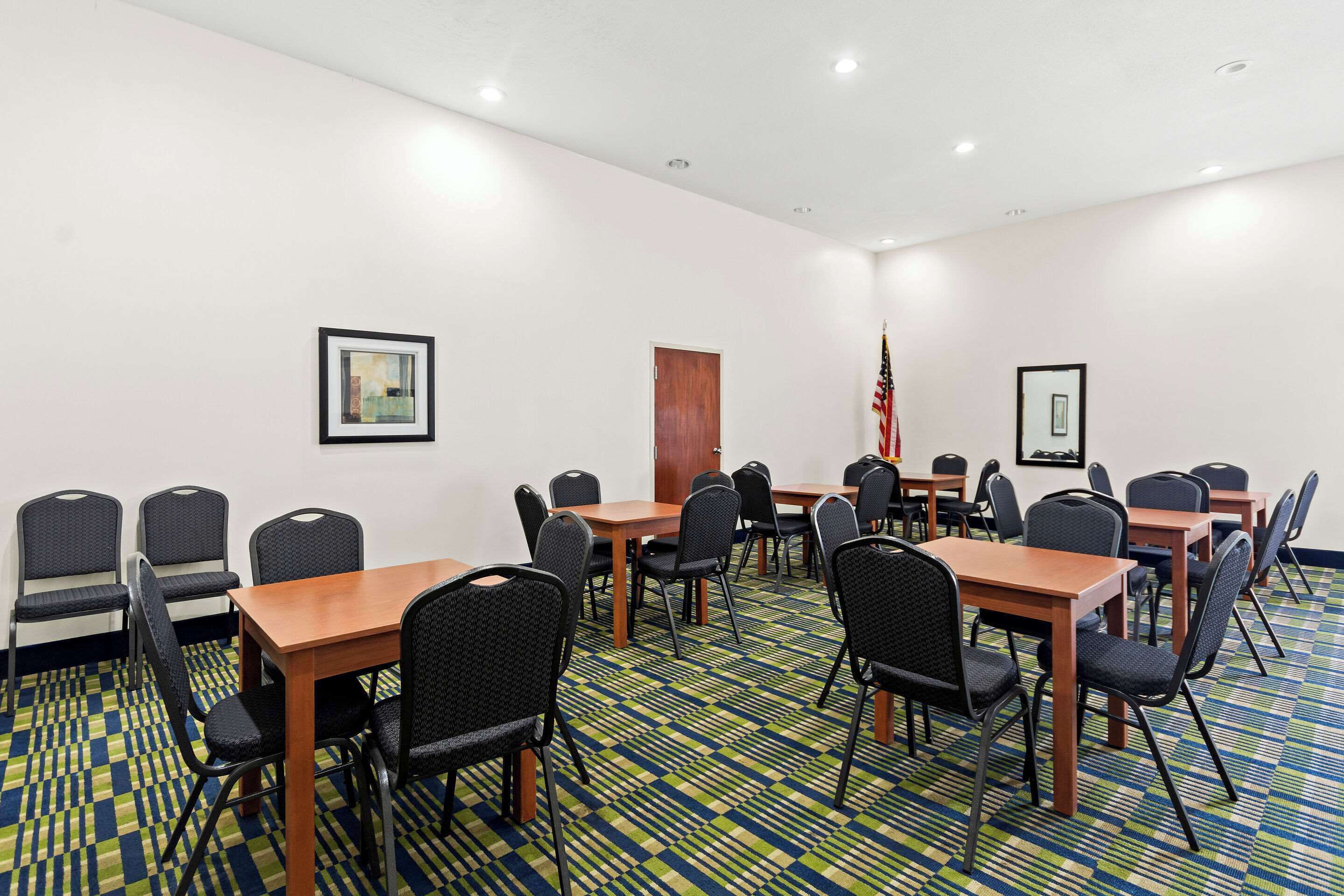 Un salón de conferencias con varias mesas y sillas, una alfombra estampada y cuadros en las paredes.