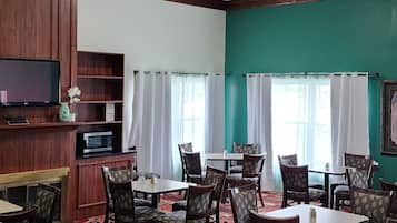 Un espace repas comprenant plusieurs tables et chaises, des ventilateurs de plafond et un téléviseur.