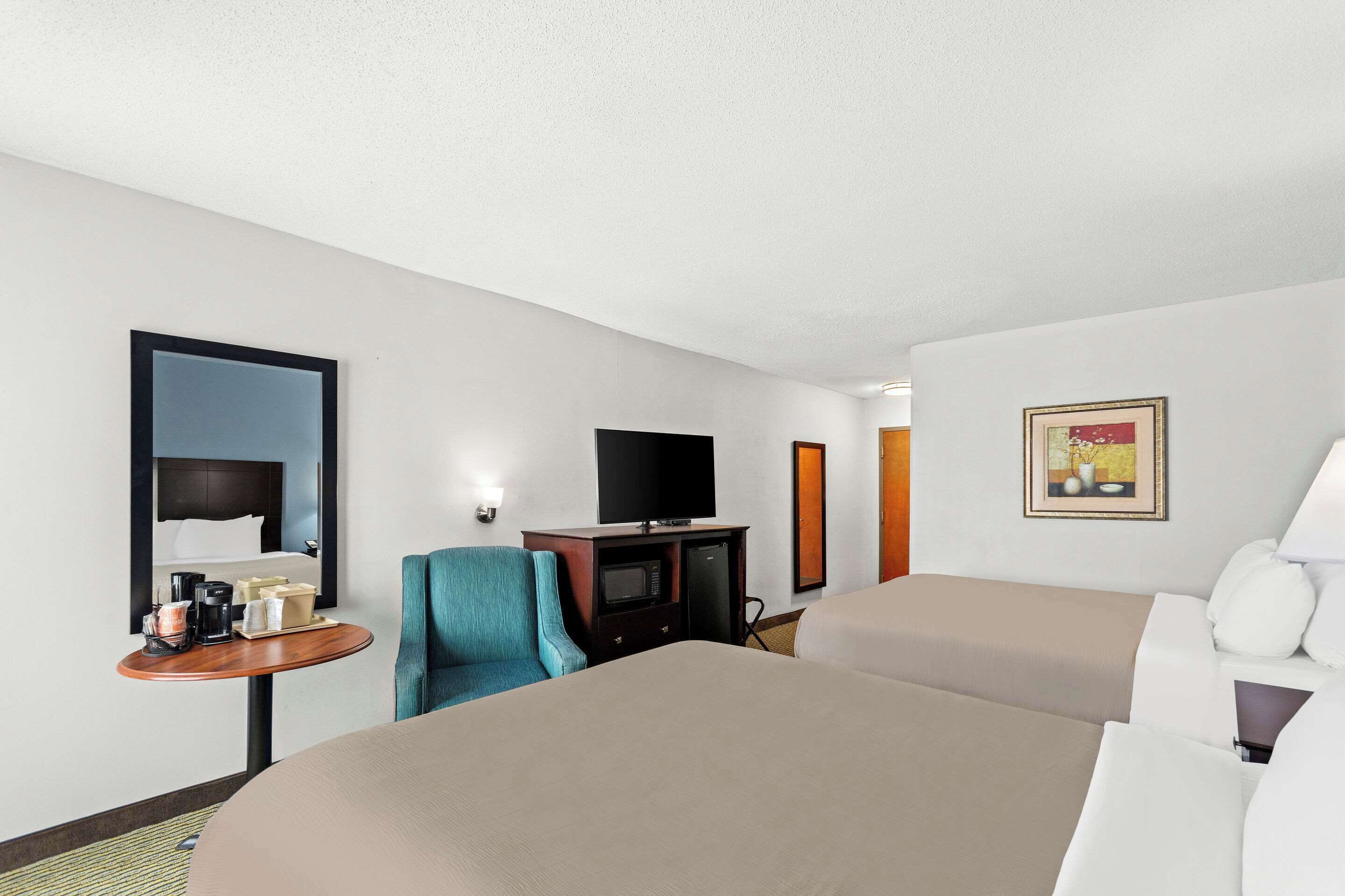 A hotel room with two beds, a desk with a flat-screen TV, a small table with a coffee maker, and a painting on the wall.