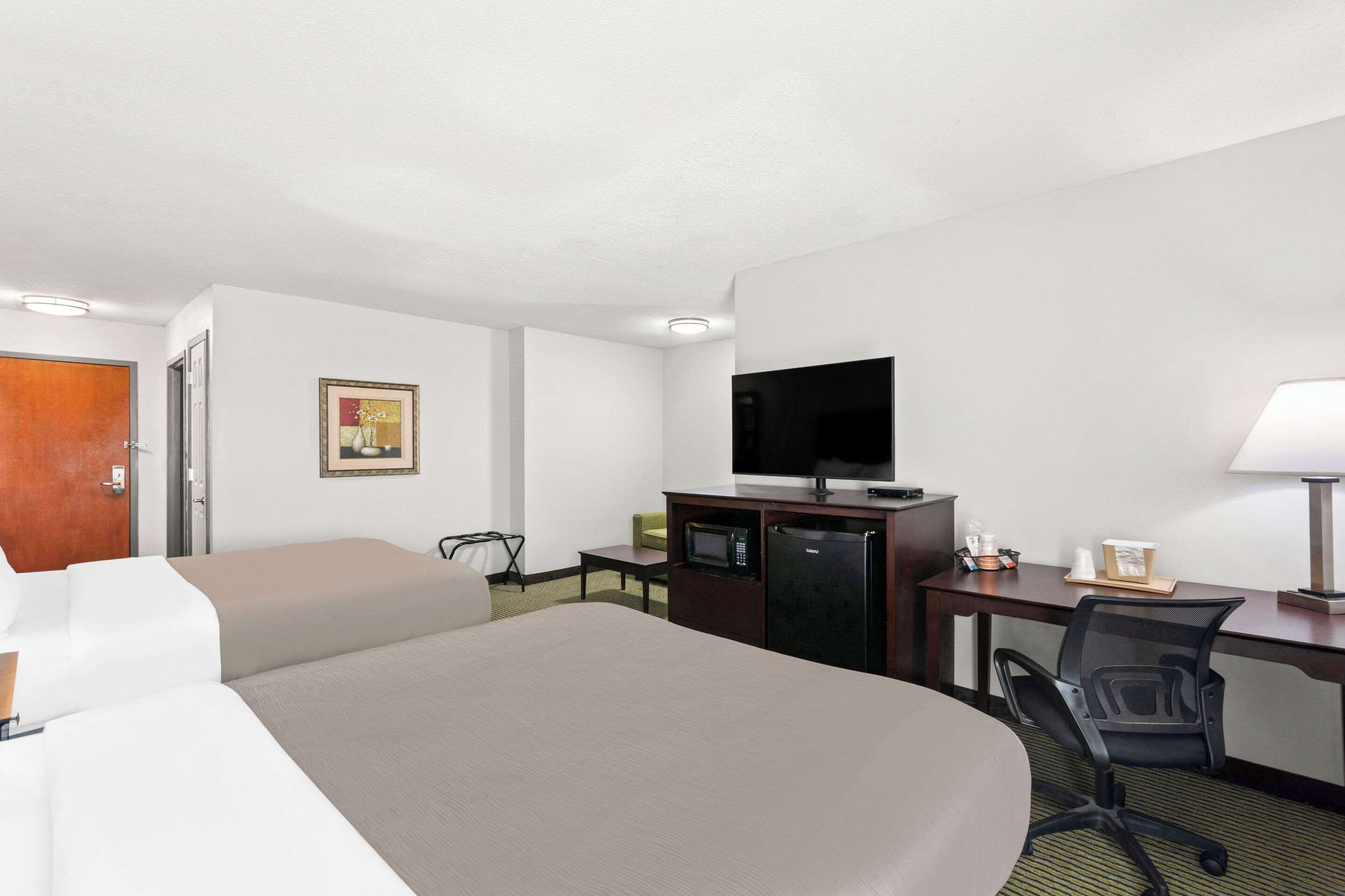 Quarto de hotel com cama, escrivaninha, televisão, micro-ondas e uma cadeira.
