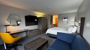 A modern hotel room with a bed, a desk, a chair, and a sofa.