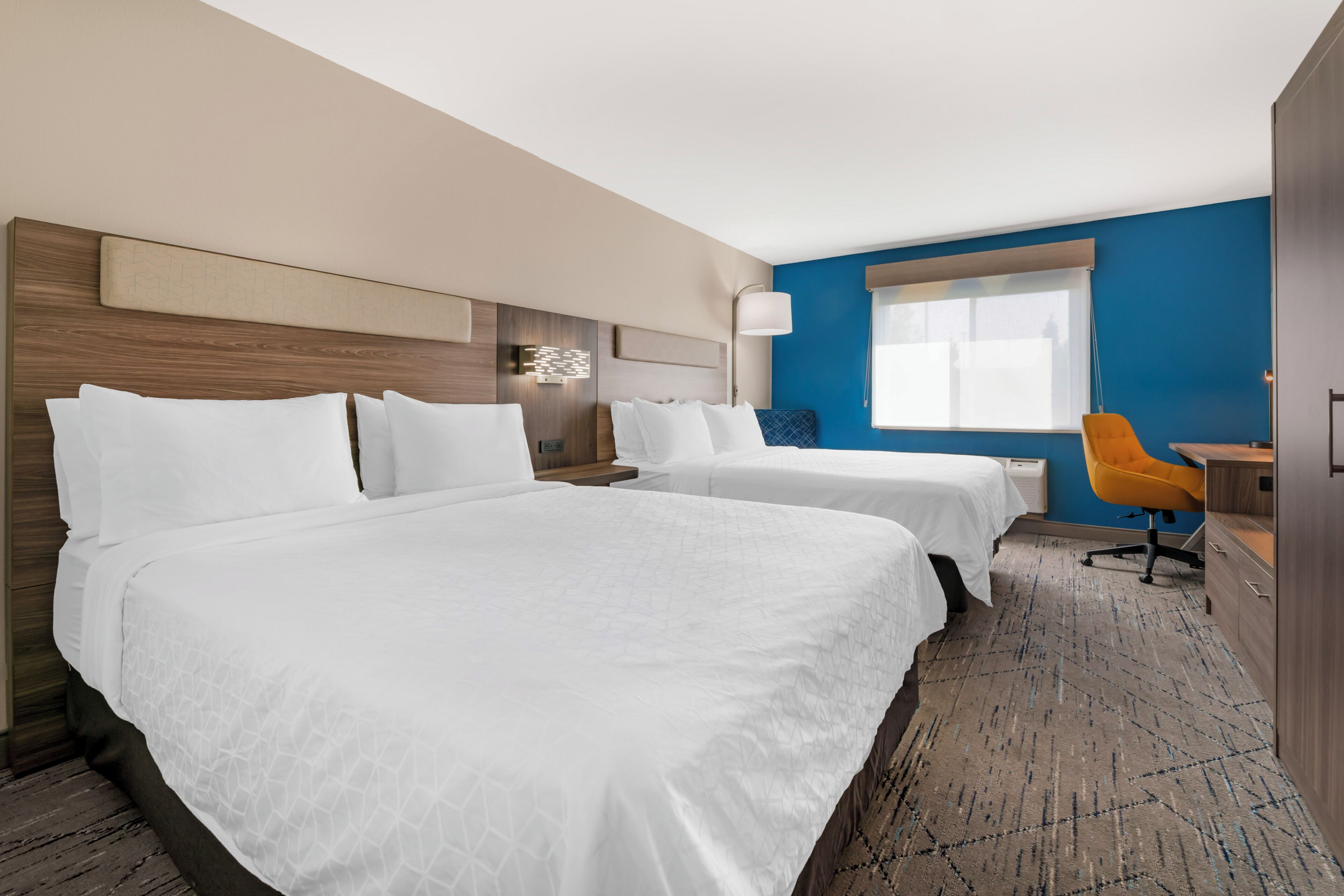 A hotel room with two beds, a desk, a chair, and a window.