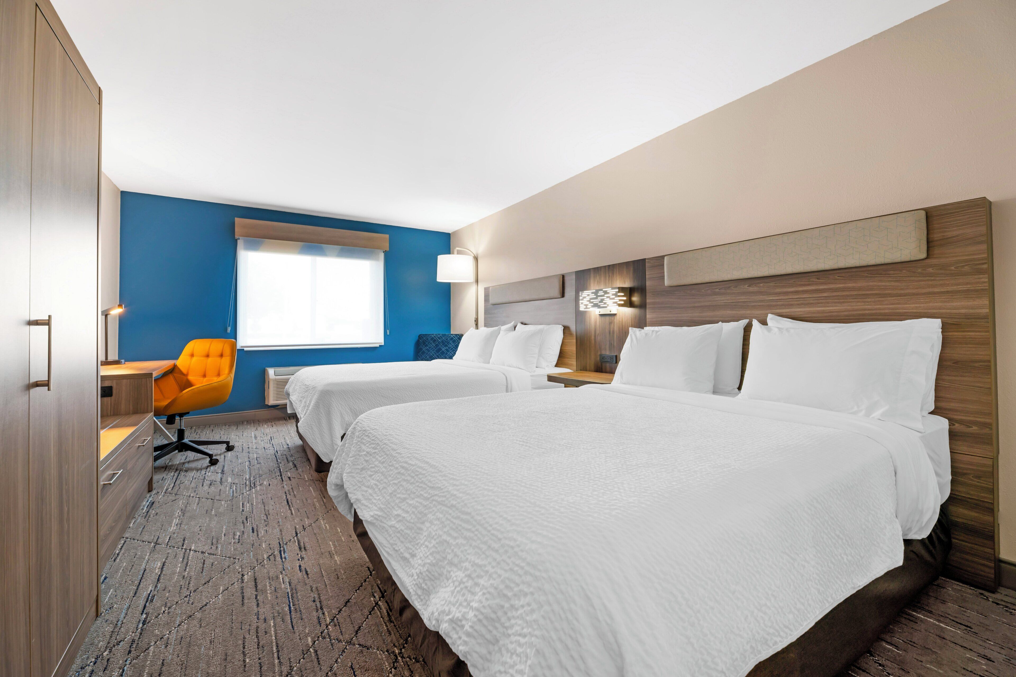 A hotel room with two beds, a desk, a chair, and a window with blinds.
