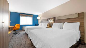 A hotel room with two beds, a desk, a chair, and a window with blinds.