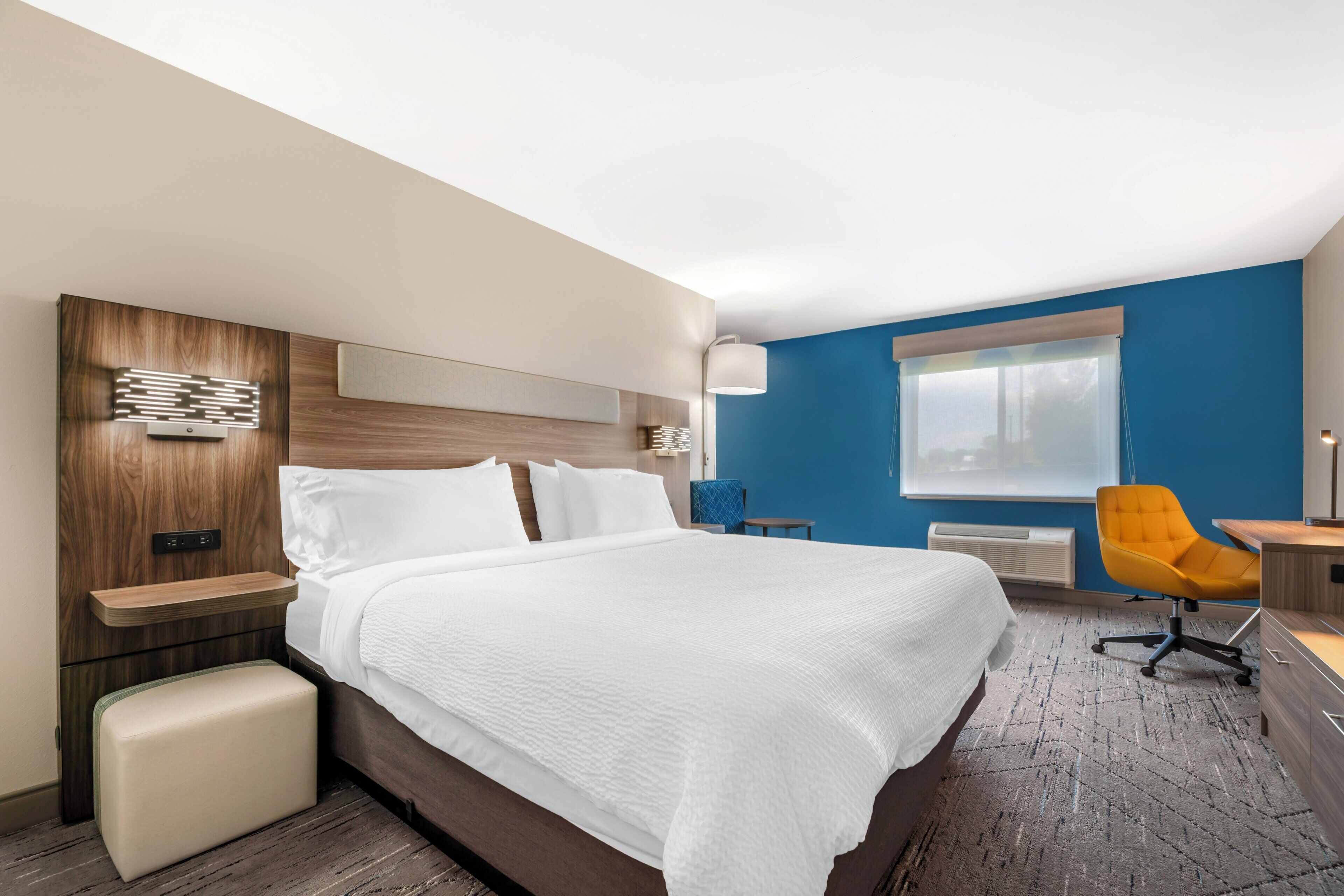 A hotel room with a large bed, a desk, a chair, and a window.